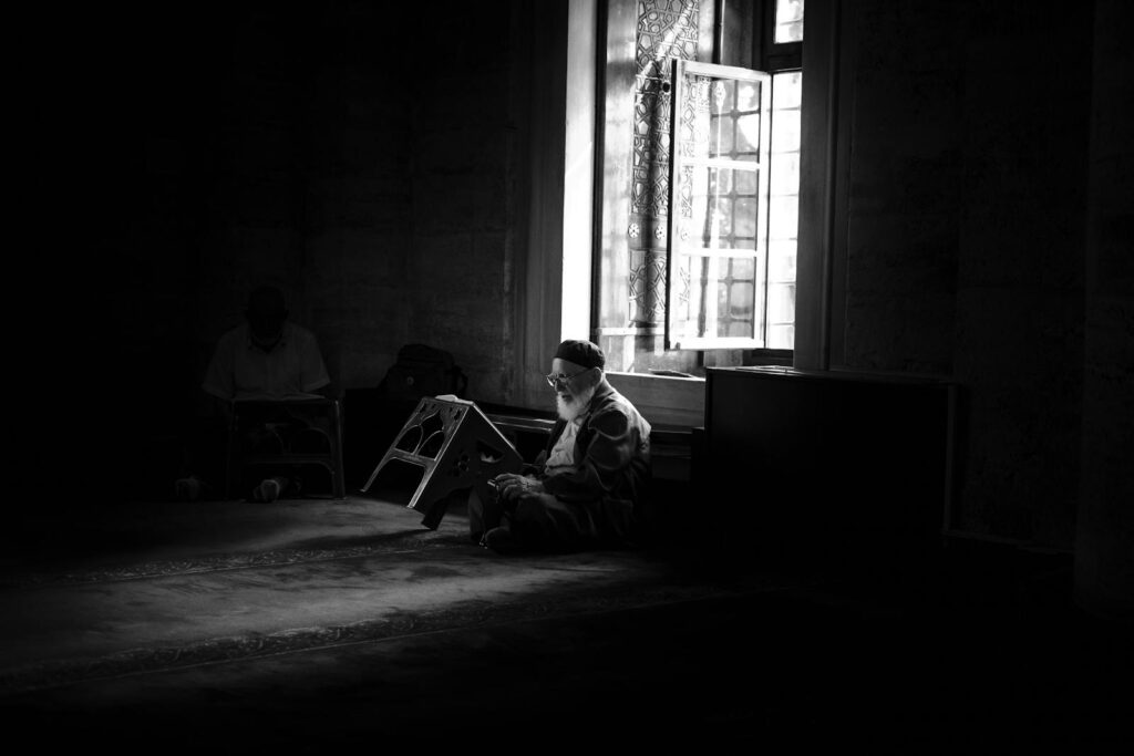 A man reading by a window in a dimly lit historic mosque in İstanbul.