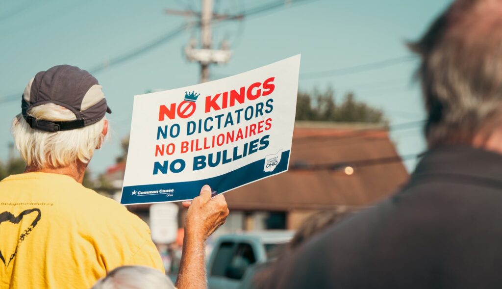 Protestor holds a sign reading 'No Kings, No Dictators' at an outdoor rally, emphasizing resistance against authoritative figures.